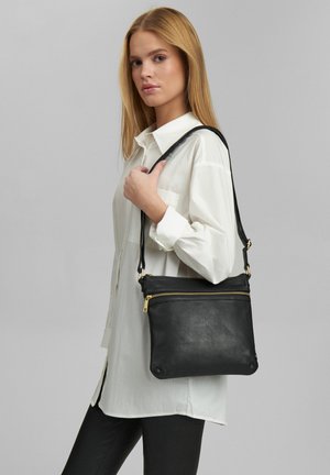 Fekete bőr crossbody táska texturált felülettel, arany cipzár részletekkel és karcsú kialakítással. Egy állítható pánttal rendelkezik.