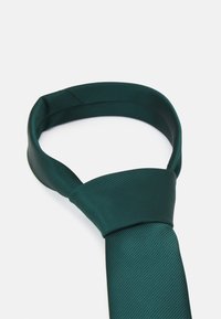 Cravate en soie verte avec un motif de rayures diagonales texturé. La cravate est soigneusement nouée en haut, mettant en valeur une finition lisse.
