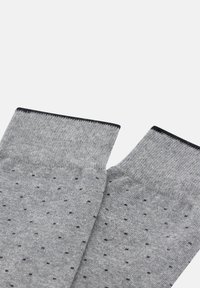 Calcetines grises hechos de un material suave con un sutil patrón de puntos en negro. Los puños están bordeados con una banda negra sólida.
