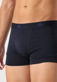 Čierne bavlnené boxerky so priliehavým dizajnom, so žltým logom Adidas na páske a hladkou, mierne textúrovanou tkaninou.