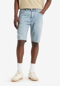 Light blue denim shorts with a relaxed fit, five pockets, and frayed hem. Paired with a beige t-shirt and white socks, worn with cream sneakers.