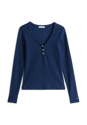 Tricou lung cu mânecă, culoare bleumarin, din material cu pliuri, cu decolteu în V, cinci butoane aurii la baza și fante laterale pentru ușurința mișcării.