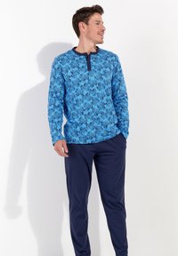 Blaues langärmliges Hemd mit floralem Muster und dunklem Kragen, kombiniert mit navyblauen Hosen in lockerer Passform. Weicher Stoff.