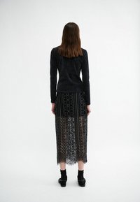 Black corduroy long-sleeve top paired with a sheer black lace midi skirt featuring intricate patterns and scalloped hem. Black ankle boots.