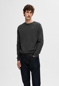 Dark gray sweater made of soft material, featuring a round neckline and long sleeves. Paired with dark blue denim jeans.