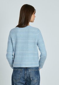 Maglione lavorato a maglia azzurro chiaro con un motivo testurizzato, scollo rotondo e maniche lunghe, abbinato a jeans in denim.