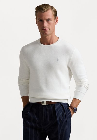 Pull blanc texturé avec des poignets et un ourlet côtelés, arborant un petit logo brodé sur la poitrine. Associé à un pantalon bleu marine à rayures.