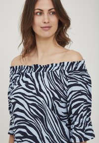 Off-shoulder topp i ljusblått och marin med zebramönster, med rynkad halsringning och trumpetärmar, tillverkad av lättviktigt tyg.