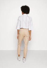 Camisa blanca recortada con rayas verticales multicolores, combinada con pantalones beiges ajustados y zapatillas blancas. Amplía un look moderno y casual.