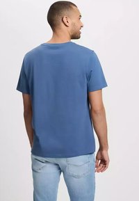 Niebieska bawełniana koszulka z okrągłym dekoltem i krótkimi rękawami, widoczna od tyłu. Noszona z jasnymi dżinsami. Gładka tekstura.