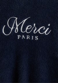Tummansininen neulepaita, joka on valmistettu pehmeästä ja karheasta materiaalista. Paita on varustettu valkoisella kirjailulla, jossa lukee "Merci Paris" kauniilla kursiivilla.