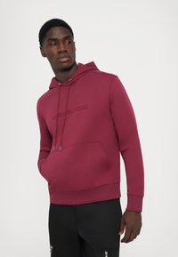 Burgunderfarget hettegenser med kengurulomme, ribbede mansjetter og brodert logo på brystet, laget av et glatt, elastisk stoff.