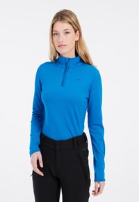 Blå långärmad tröja med hög krage, halvdragkedja, slät yta, och svarta byxor med bälte och fickor med dragkedja.