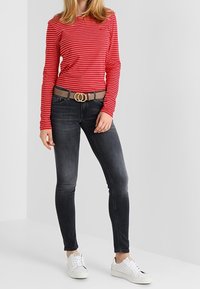 Camisa de manga larga a rayas rojas y blancas, vaqueros ajustados grises, cinturón marrón con hebilla redonda dorada, zapatillas blancas con detalle perforado.