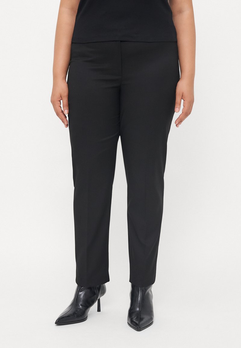 Black tailored pants with a smooth texture, slim fit, and a mid-rise waist, paired with black pointed-toe ankle boots.