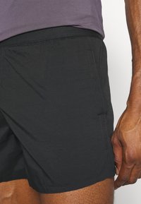 Pantalones cortos deportivos negros con cintura elástica, que presentan una textura suave y bolsillos laterales, con costuras visibles a lo largo de los bordes.