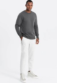 Felpa grigia con scollo rotondo, abbinata a pantaloni bianchi aderenti e sneaker alte grigie in tonalità neutra. Design semplice con polsini a costine.