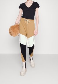 Color-blocked joggers in tan, black, and white with elastic cuffs, paired with a black V-neck tee and cream platform boots, carrying a fluffy bag.