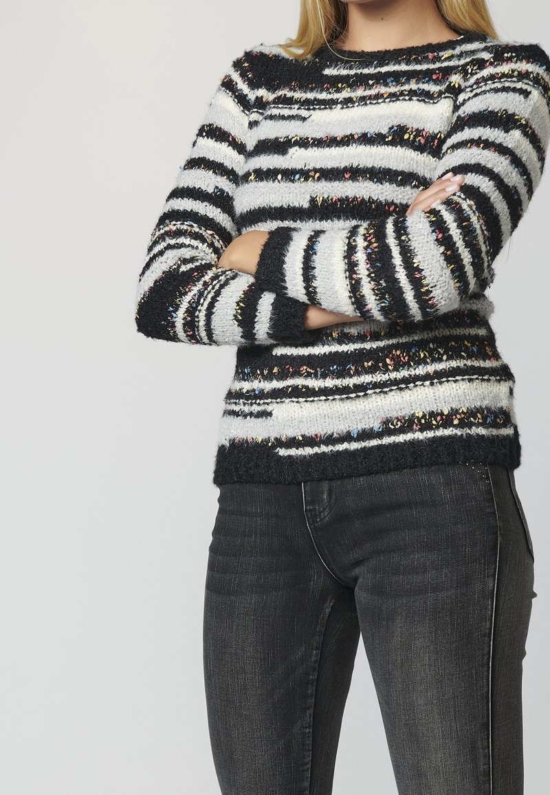 Black and white striped sweater with multicolored flecks, knit texture, crew neckline, and fitted sleeves; paired with dark jeans.