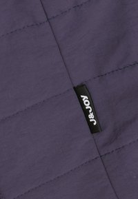 Paarse stof met een gestructureerde afwerking, met zichtbare stiksels en een zwart label met witte tekst "J&JOY."