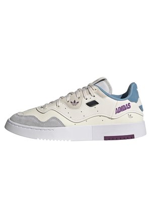 Baskets basses Adidas en crème, suède gris et bleu avec marquage violet et semelle blanche épaisse à grip texturé.