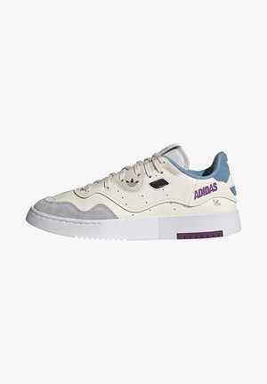 Baskets basses Adidas en crème, suède gris et bleu avec marquage violet et semelle blanche épaisse à grip texturé.