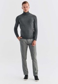 Ciemnoszary sweter w serek z gładkiego materiału, zestawiony z jasnoszarymi, fakturowanymi spodniami o slim fit oraz czarnymi sneakerami.