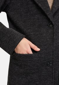 Textured zwarte jas met een verticale streeppatroon, voorzien van een gesneden kraag, enkele knoopsluiting en een zijzak.
