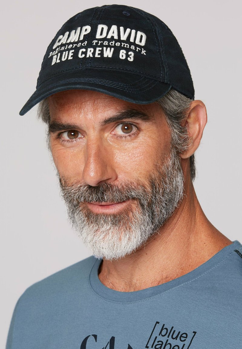 Granatowa czapka bejsbolowa z białym haftowanym napisem "CAMP DAVID" i "BLUE CREW 63". Jasnoniebieski t-shirt z okrągłym dekoltem z czarnym nadrukiem graficznym.