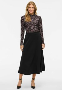 Černá sukni zabalena do tvaru s dlouhým rukávem, přiléhavým topem s růžovým leopardím vzorem. Tkanina vypadá měkká s hladkým povrchem.