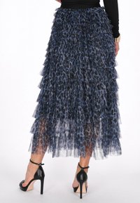 Egy nő, aki kék és fekete leopárdmintás tüll szoknyát visel, fekete magassarkú bokapántos szandállal, hátulról látható.