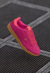 Lys rosa sneaker med overdel i semsket skinn, gummisåle og kontrasterende oransje detaljer på kragen og snøringene. Gulllogo detalj på siden.