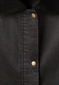 Tkanina z leopardjim vzorom v temno rjavi barvi z teksturiranim črnim kordom. Ima vrsto okroglih zlatih pritisnjenih gumbov.