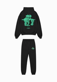 Zwarte hoodie en joggingbroek set met een groene afbeelding van een beer en tekst op de achterkant en voorkant. Gemaakt van katoenmix, met een ontspannen pasvorm.