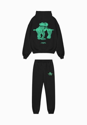 Zwarte hoodie en joggingbroek set met een groene afbeelding van een beer en tekst op de achterkant en voorkant. Gemaakt van katoenmix, met een ontspannen pasvorm.
