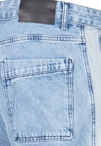 Jeanși din denim de culoare albastru deschis, cu un buzunar pe spate, cusături vizibile și o etichetă din piele la talie cu logo embosat.