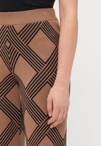Bruine gestreepte broek met een geometrisch zwart ontwerp met diagonale lijnen. Zachte textuur met een geribde tailleband voor extra comfort.