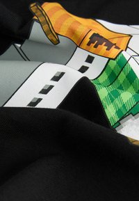 Čierna látka s hladkým povrchom, so farebným grafickým dizajnom obsahujúcim oranžové, zelené a šedé prvky v zloženom stave.