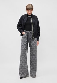 Black bomber jacket over a black turtleneck, paired with high-waisted, wide-leg gray patterned pants featuring a tie waistband.