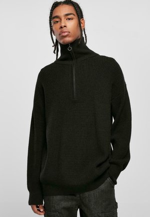 Pull en maille côtelée noir avec un col montant et une fermeture éclair quart, doté de manches longues et d'une coupe décontractée. Le tissu texturé ajoute de la profondeur.