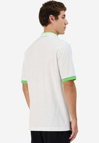 Polo bianco con dettagli verdi su colletto e maniche, realizzato in tessuto traspirante, con un taglio classico e maniche corte.