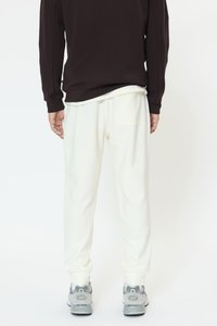 Bele trenirke s stranskim žepom, kombinirane s temno rjavo majico z dolgimi rokavi in sivimi supergami. Mehka tekstura, sproščen kroj.