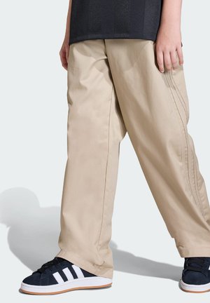 Béžové volné kalhoty z lehké tkaniny s vertikálními švy a širokými nohavicemi. Kombinovány s námořnicky modrými teniskami s bílými pruhy.