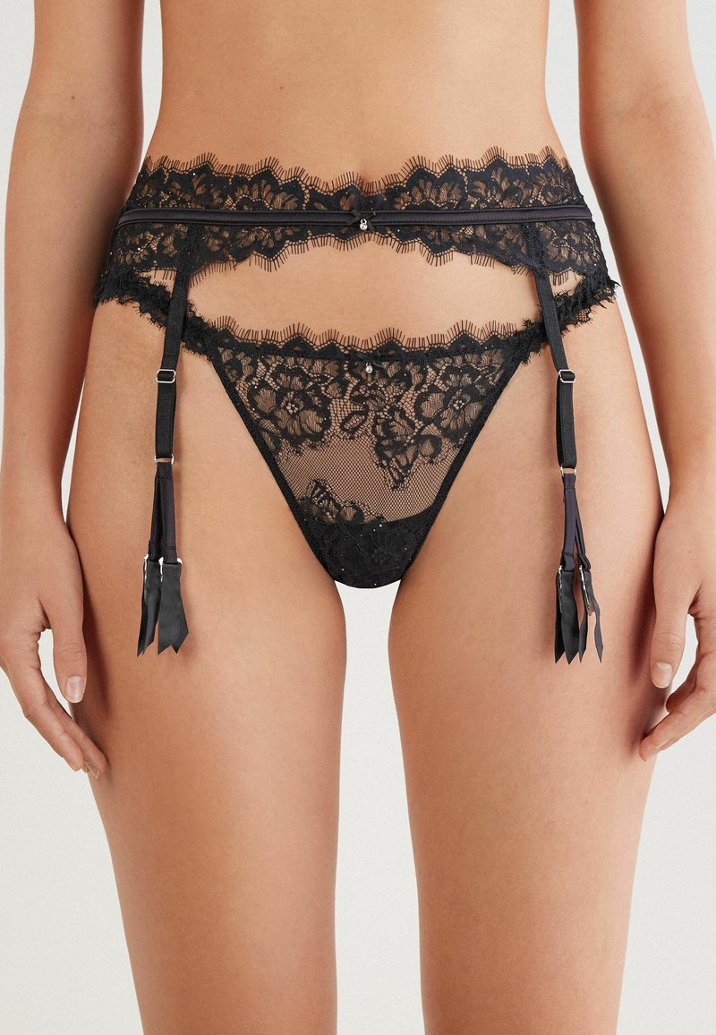 Svart spets garterbälte och trosor set med blommönster, volangkanter, justerbara band och svarta satängsnyggningar.