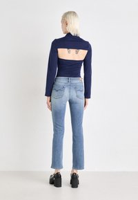 Navy long-sleeve top with open back, paired with mid-rise light blue jeans featuring rear pocket stitching. Black chunky heeled shoes.