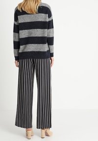 Randig grå och marinblå tröja med avslappnad passform, i kombination med vida marinblå byxor med vertikala vita ränder och beige klackar.