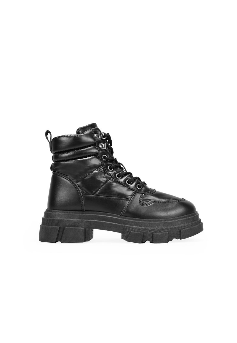Botas negras de tobillo con una suela gruesa, hechas de cuero brillante. Cuentan con un cierre de cordones en la parte delantera, un cuello acolchado y una lengüeta en el talón.