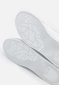 Semelles de chaussures en caoutchouc blanc présentant un motif de semelle géométrique avec des nervures texturées et une surface lisse et plate pour l'adhérence.