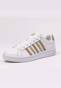 White sneaker featuring three tan stripes, a rounded toe, textured leather upper, and white rubber sole with embossed logo.