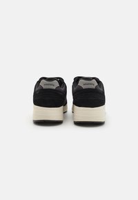 Baskets en suède noir et mesh, avec une semelle intermédiaire couleur crème et une semelle extérieure en caoutchouc noir. Présente le logo Saucony sur la languette arrière.